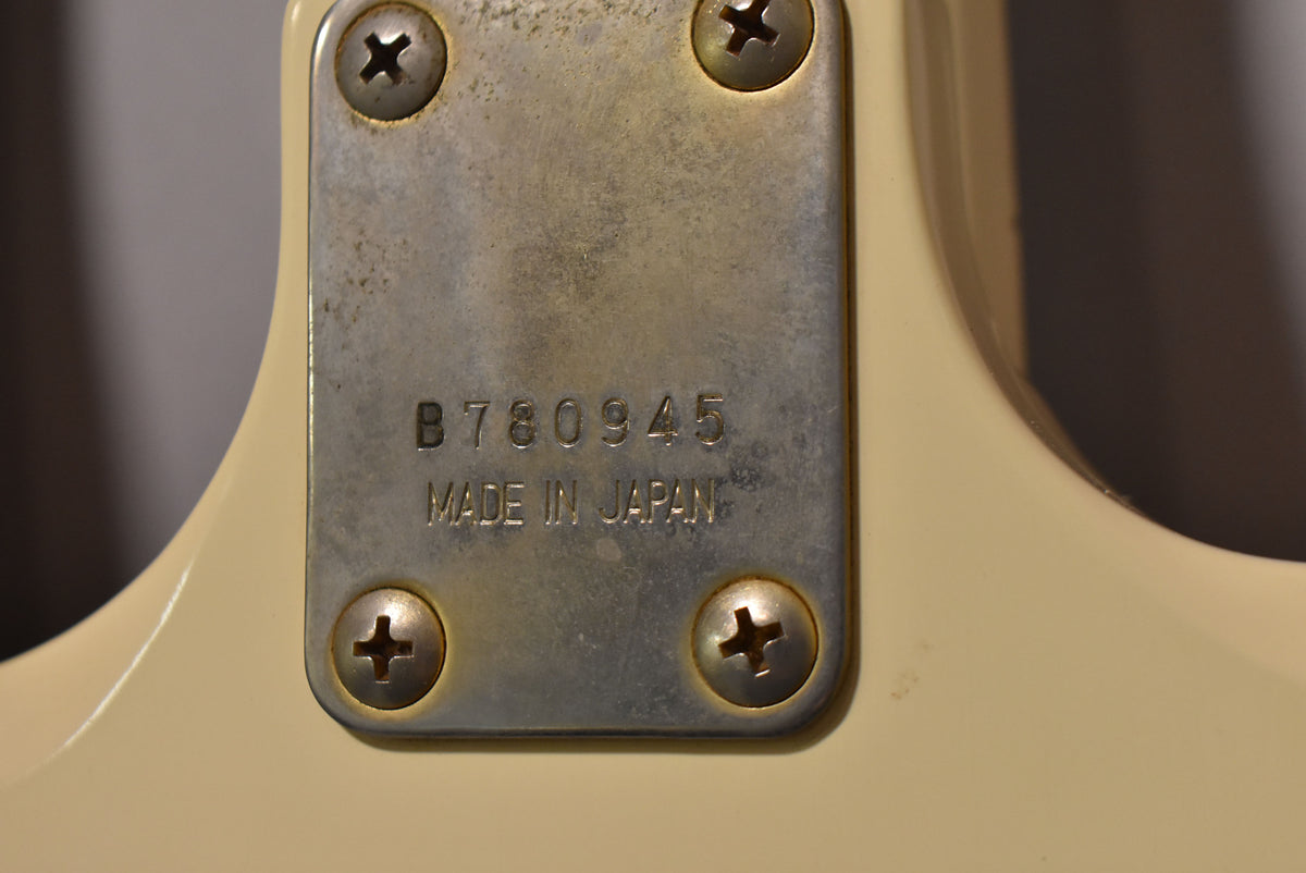 Close-up of the guitar's neck plate, showing a worn, rectangular metal plate with four Phillips head screws and stamped text.