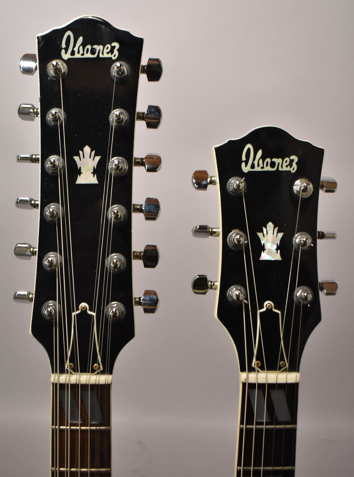 Close-up of two black headstocks with white binding, mother-of-pearl inlays, and chrome tuners, showing 12-string and 6-string necks.