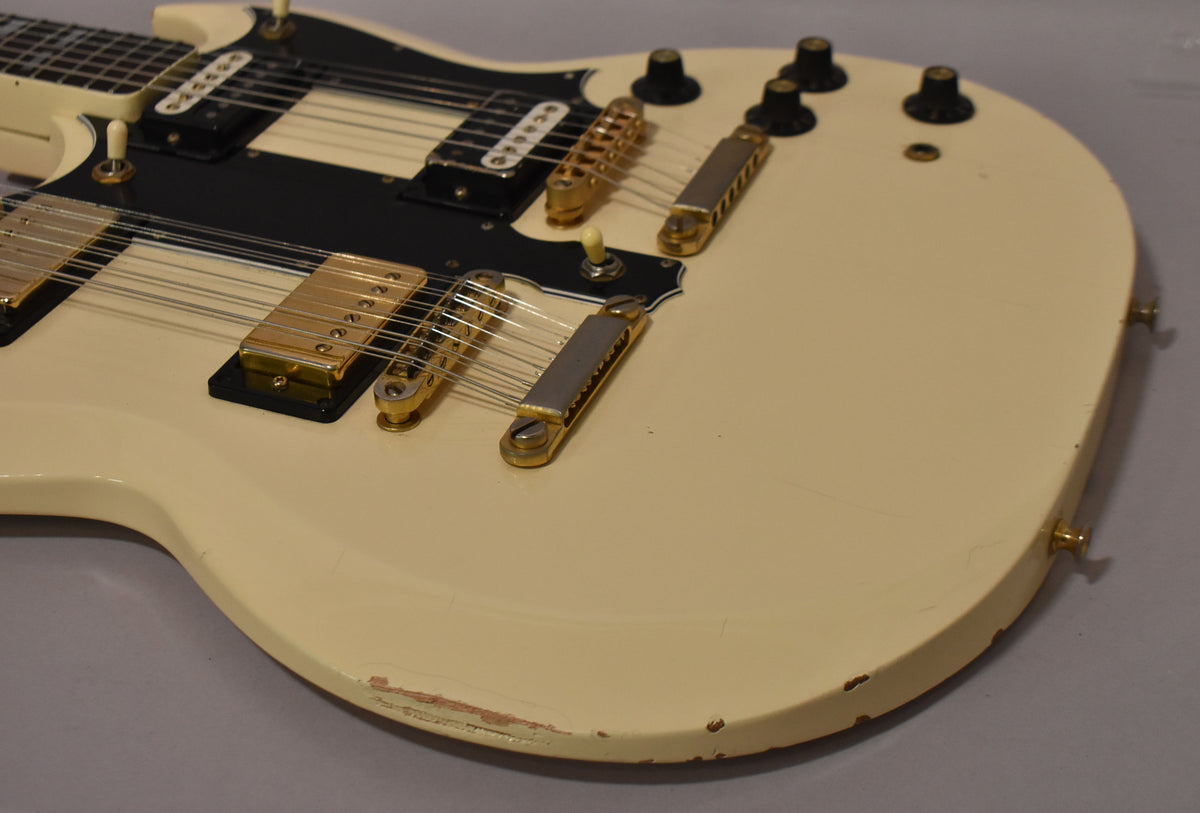 Close-up of the cream double-neck guitar body, showing gold hardware, black pickguard, and significant paint chips along the lower edge.
