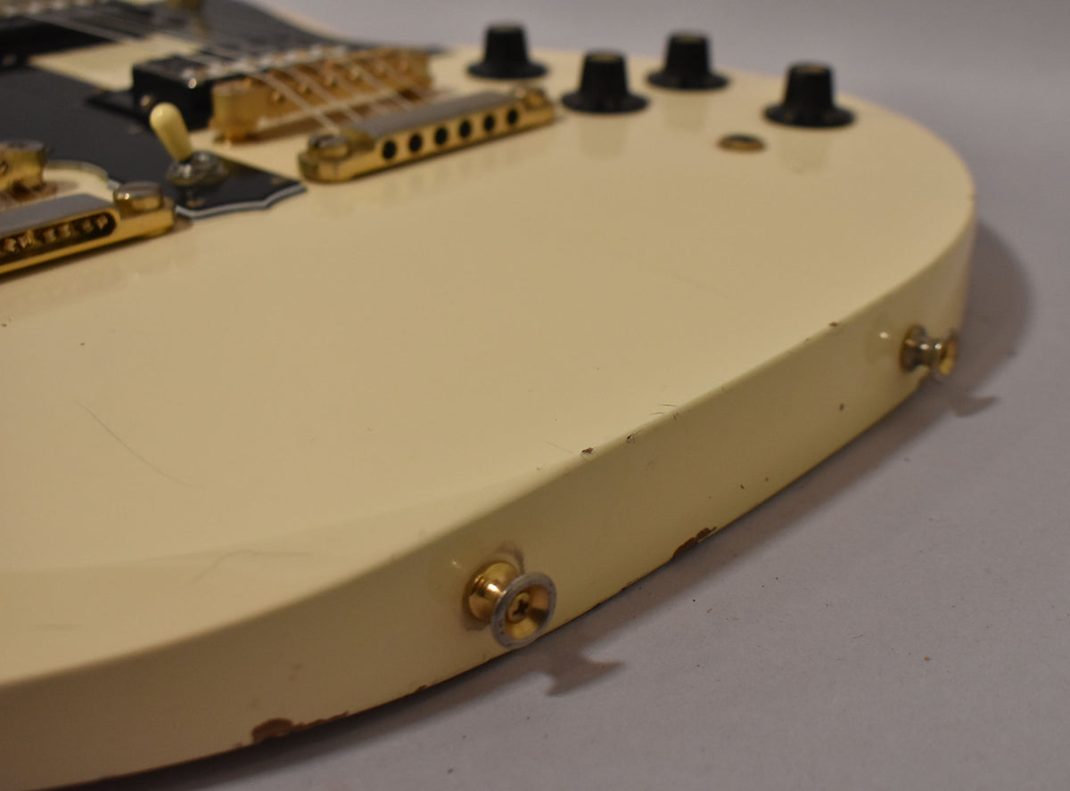 Close-up of the guitar's lower bout, showing the aged white finish, gold hardware, black control knobs, and visible chips and scratches.