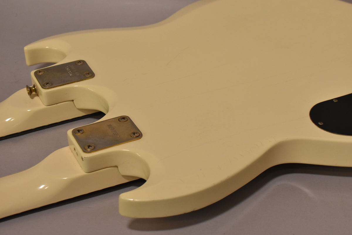 The back of the white double-neck guitar shows two neck plates, a black control cavity cover, and light scratches and wear on the finish.