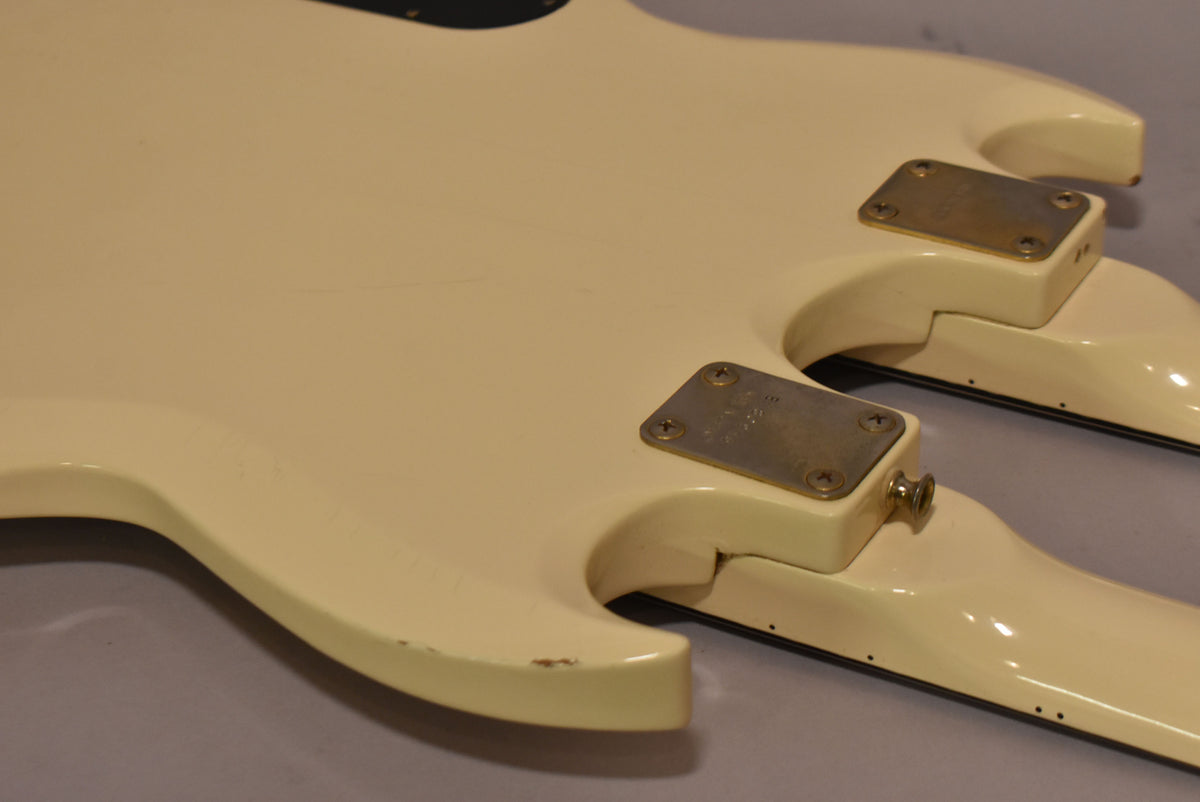 Close-up of the double-neck guitar's white body from the back, showing two brass neck plates and some finish wear on the lower horn.