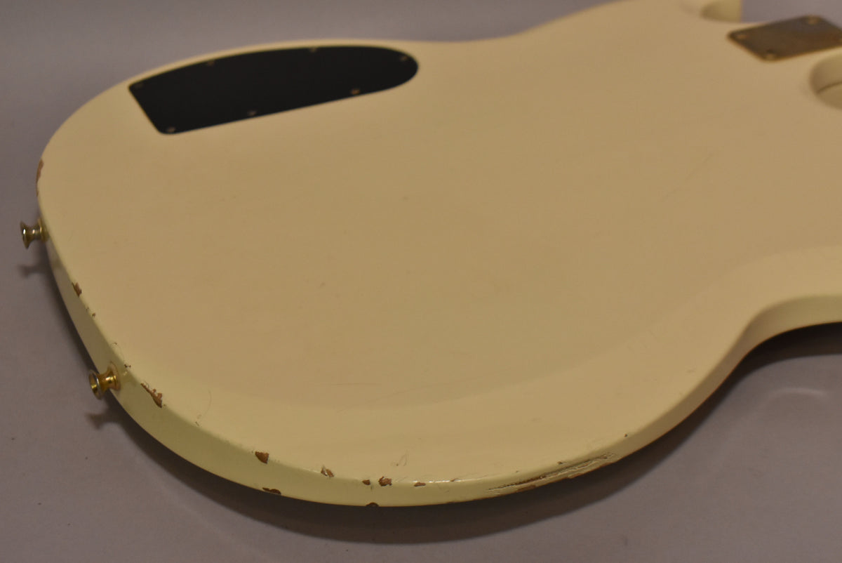 The back of the off-white double-neck guitar body, showing a black control cavity cover and significant paint chipping along the lower edge.