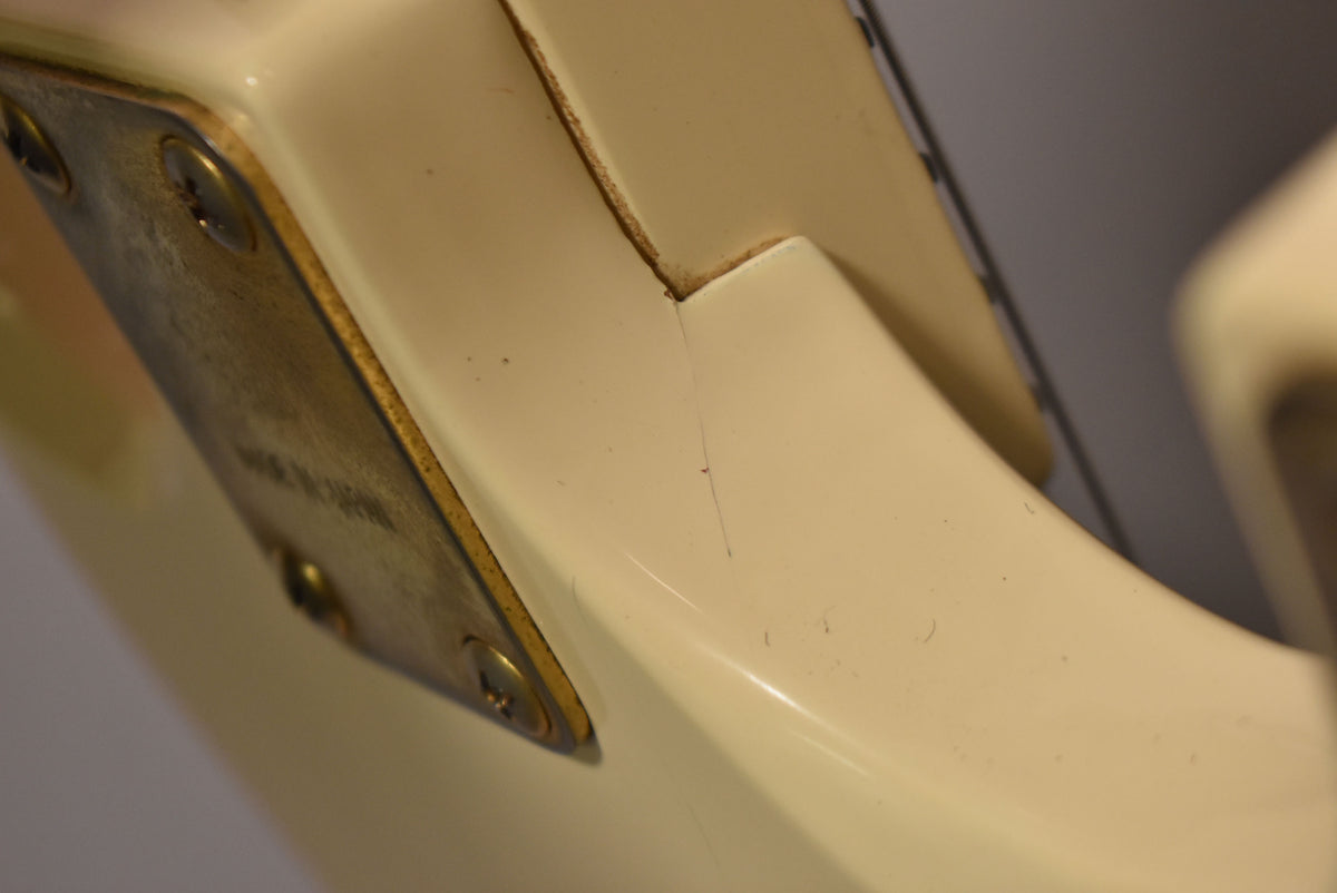 Close-up of the guitar's white body, showing a tarnished gold neck plate with three screws and a thin crack in the finish near the neck joint.