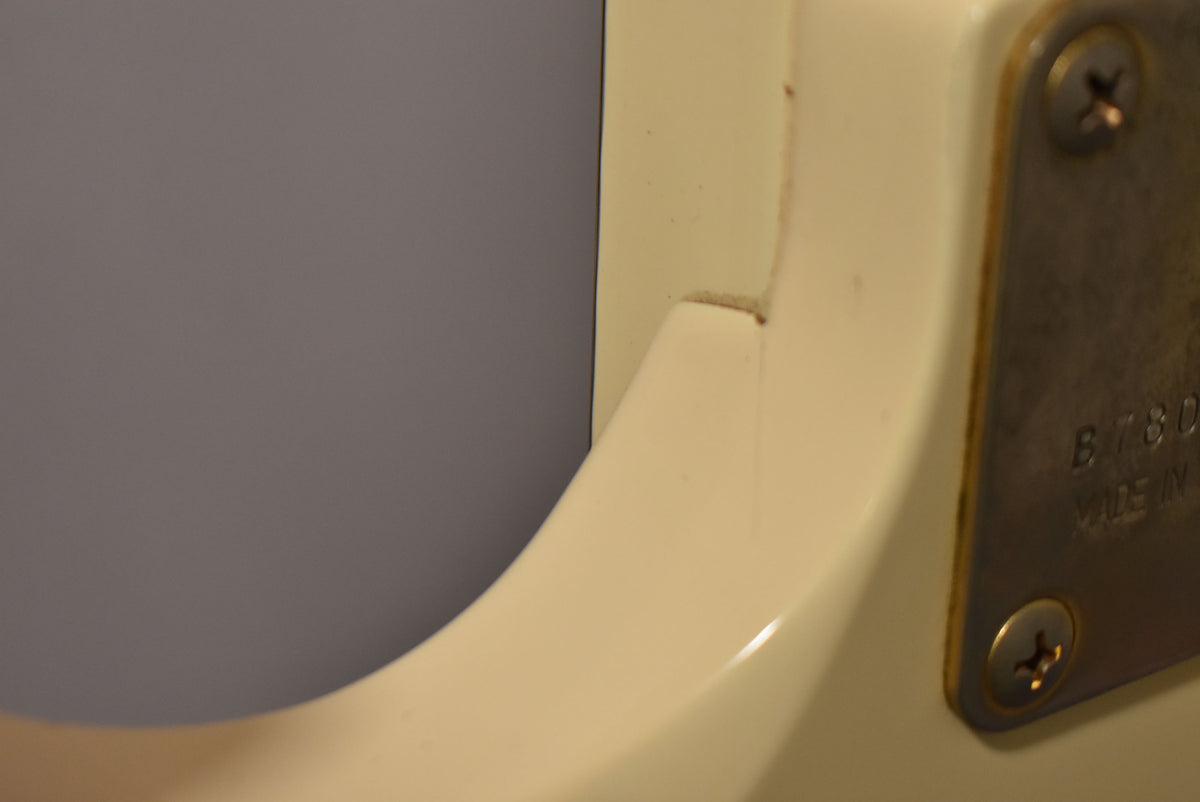 Close-up of the white guitar body's neck joint, showing a small crack in the finish and a metal neck plate with two visible screws.