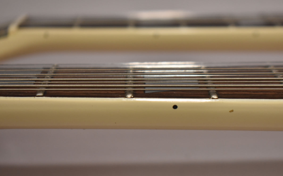 Close-up of the lower neck and fretboard, showing the white binding with a black side dot and a small chip near the fret.