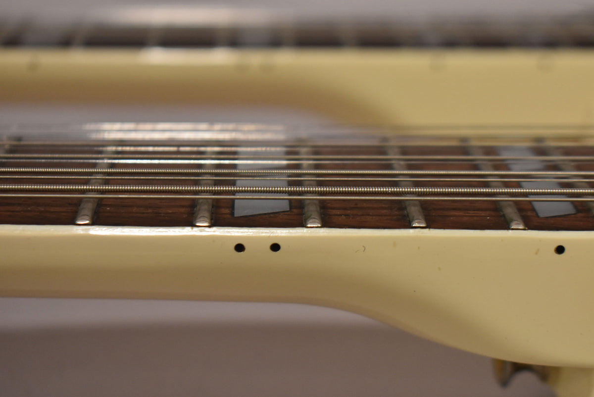 Close-up of the lower neck and fretboard of the 6-string neck, showing dark wood, trapezoid inlays, and two small holes on the side.