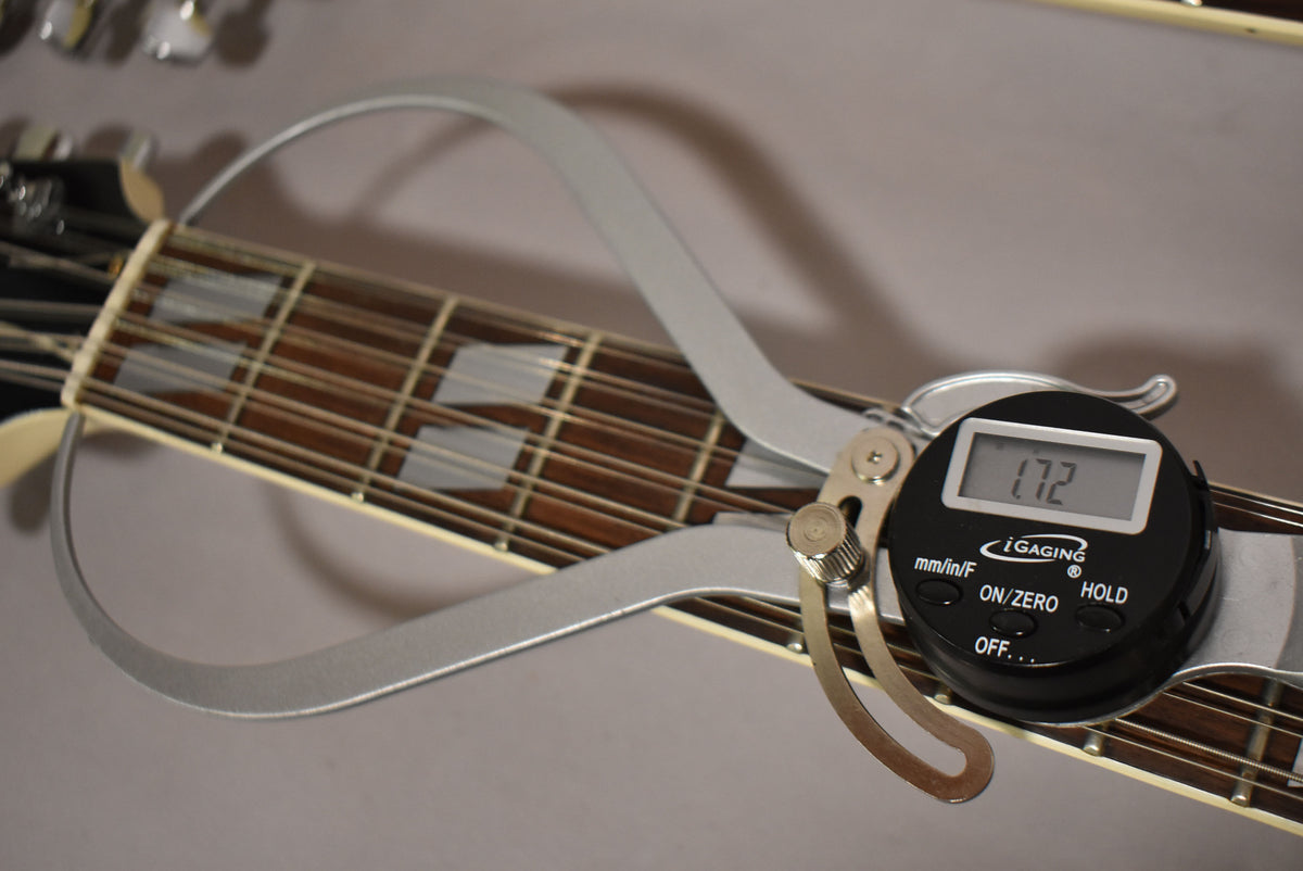 A digital caliper measures the nut width of the 12-string neck, showing 1.72, with trapezoid inlays visible on the dark fretboard.