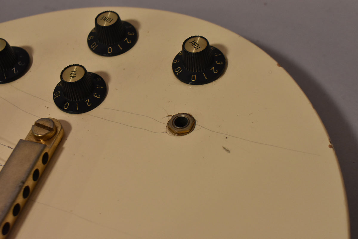 Close-up of the guitar's cream body, showing four black numbered knobs, a gold-rimmed output jack with cracks, and a gold tailpiece.