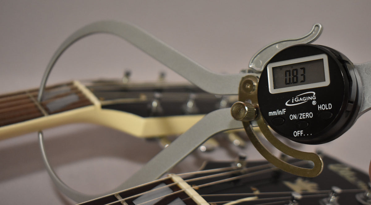A digital caliper measures the string height on the lower neck of the white double-neck guitar, showing 0.83mm.