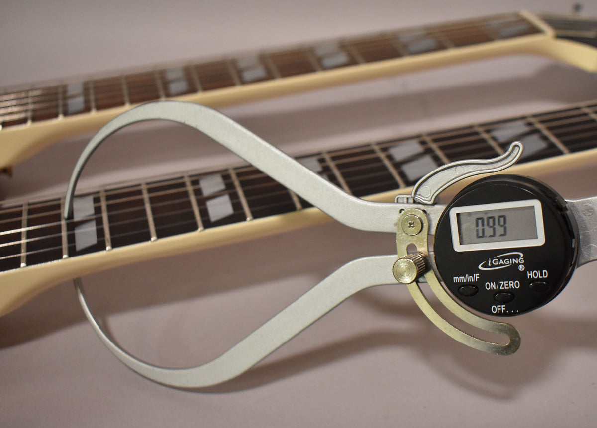 A digital caliper measures the fret height at 0.99mm on the lower neck, showing block inlays on a dark fretboard.