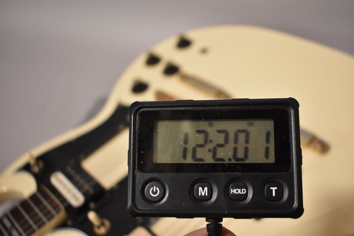 A digital scale displaying "12.20.1" obscures the white double-neck guitar's lower body and pickups.