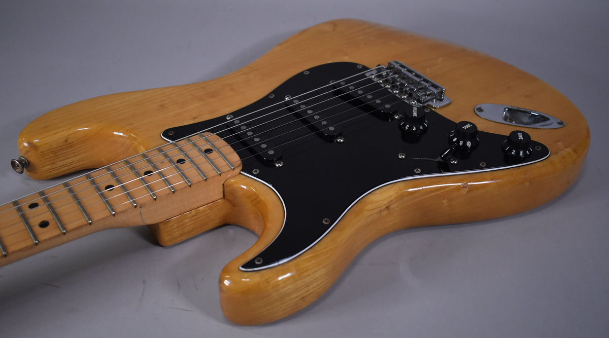 Left-handed natural finish Stratocaster body and neck, showing black pickguard, three single-coil pickups, and chrome hardware.