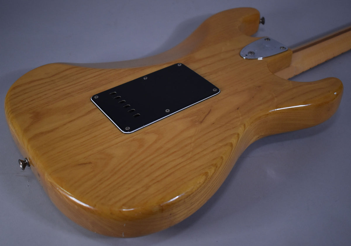 The back of the natural finish guitar body, showing the black tremolo cavity cover and chrome neck plate, with light wear.