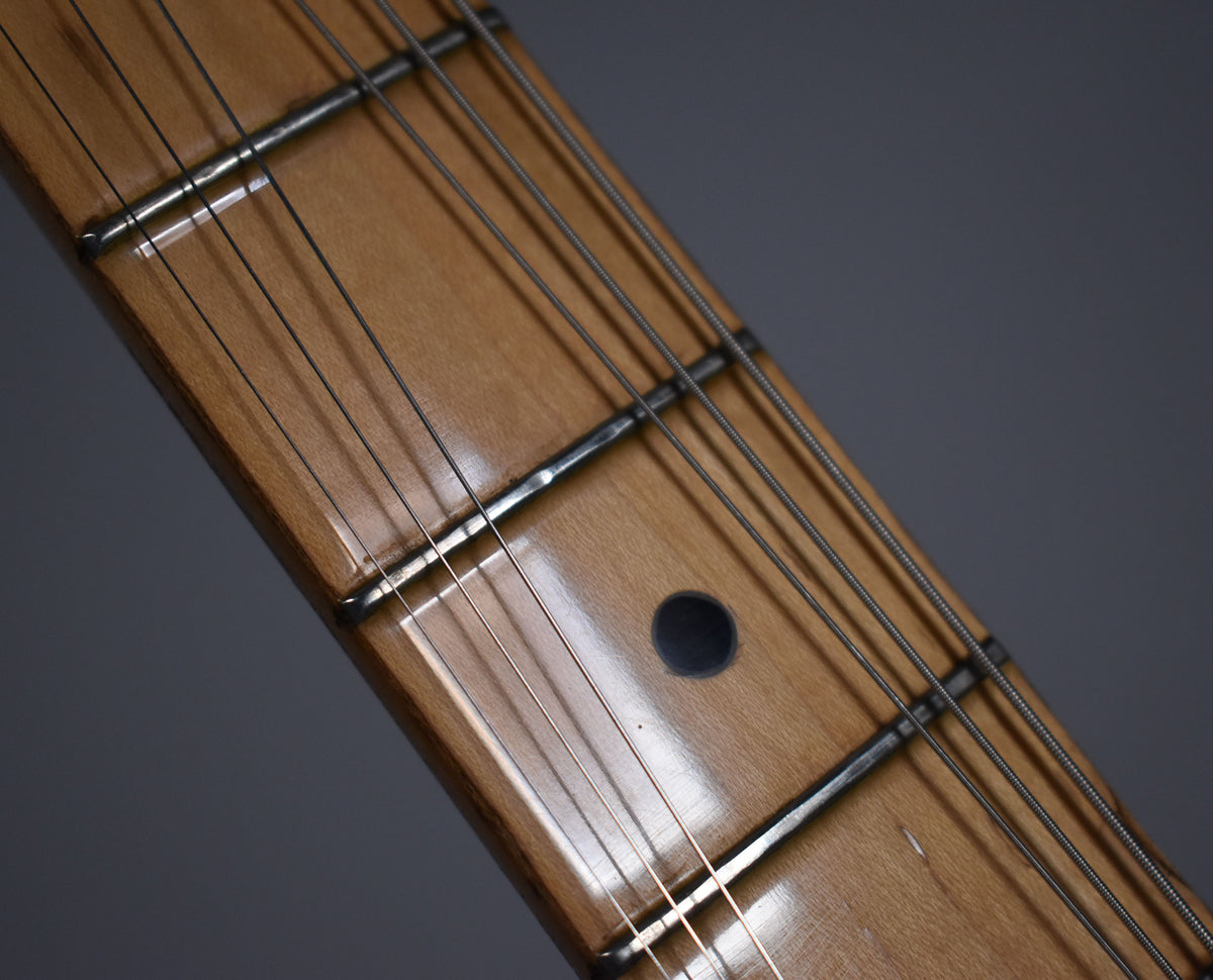 Close-up of the maple fretboard and frets, showing a dark circular inlay at the 7th fret and light wear on the wood.