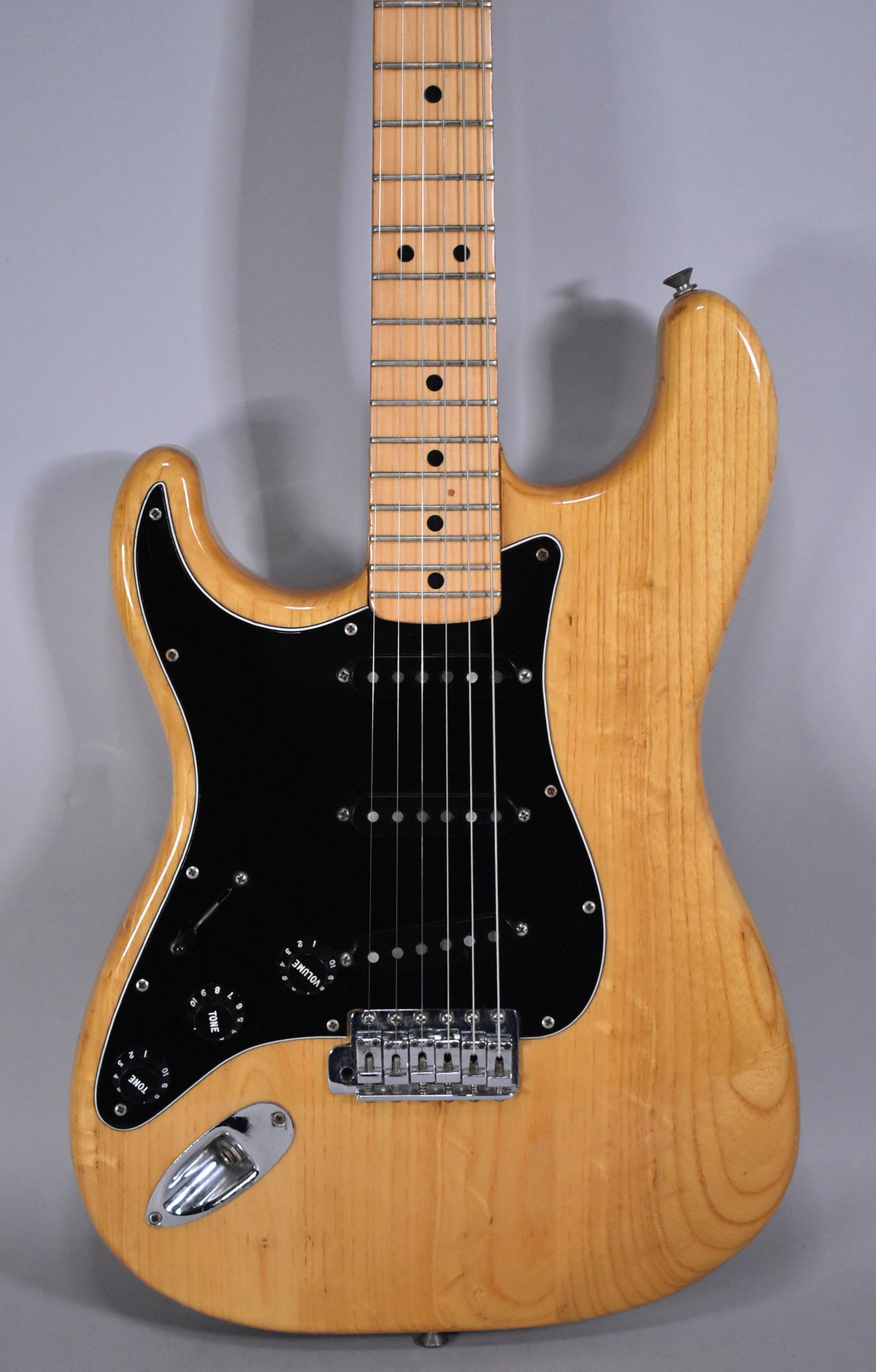 Full-frame, natural-finish left-handed Stratocaster with a black pickguard, maple fretboard, and chrome hardware.