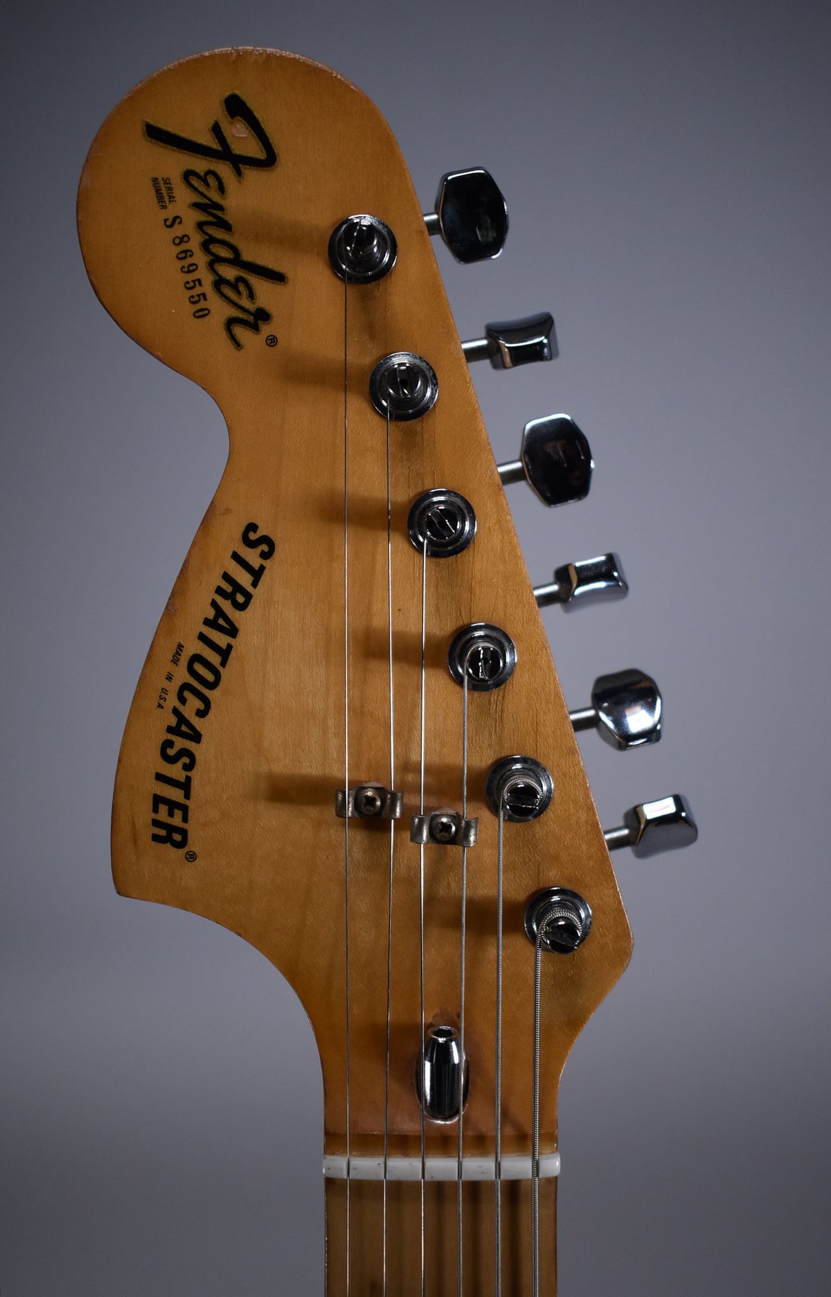 Close-up of the natural finish headstock and tuning pegs, showing some wear along the top edge and a string tree.