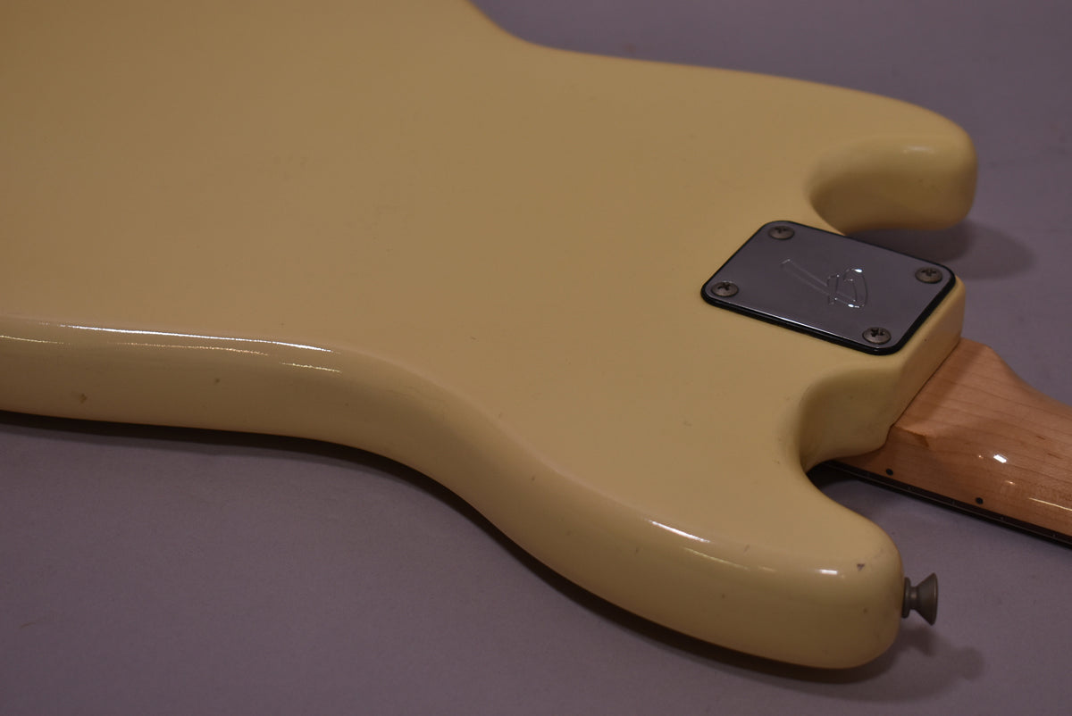The guitar's creamy white body, viewed from the back, shows a chrome neck plate, a light maple neck, and a strap button.