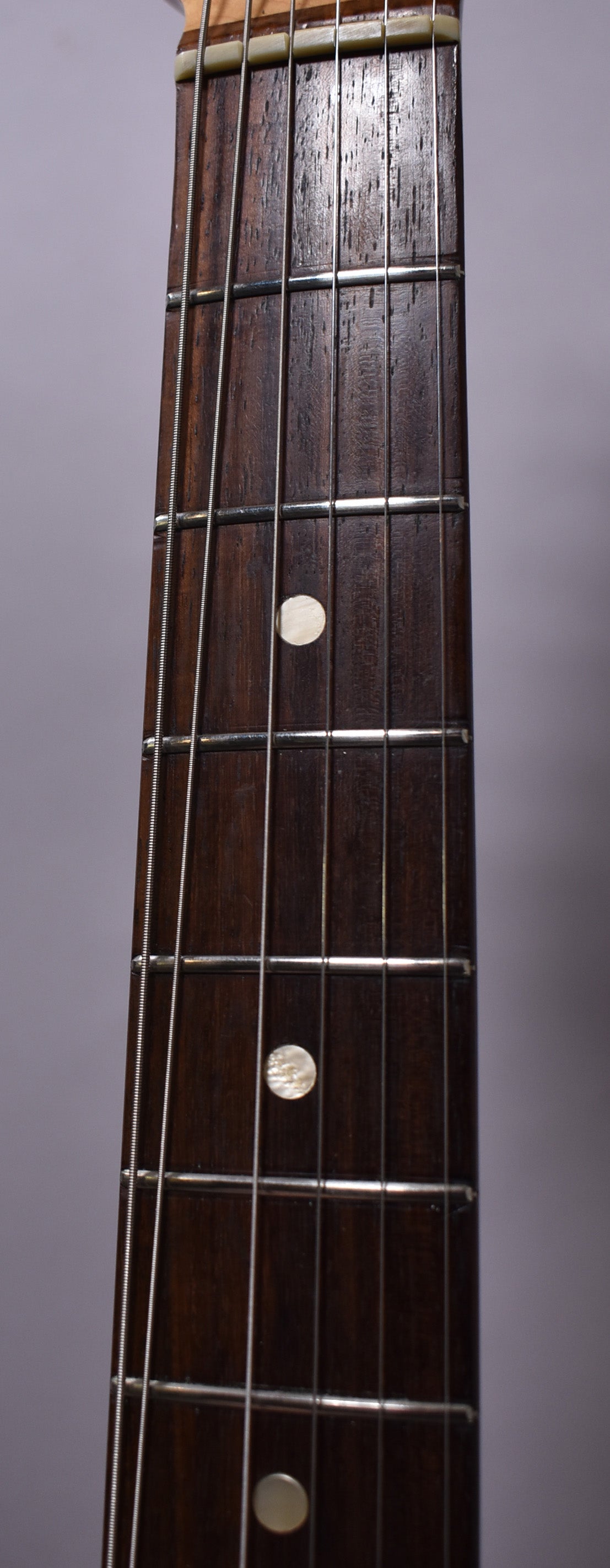 Close-up of the dark rosewood fretboard with light, circular inlays at the 5th and 7th frets, showing some wear and string grooves.