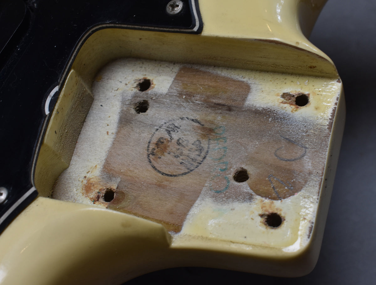 Close-up of the guitar's neck pocket, showing exposed wood, four screw holes with rust, and a faint circular stamp on the wood.