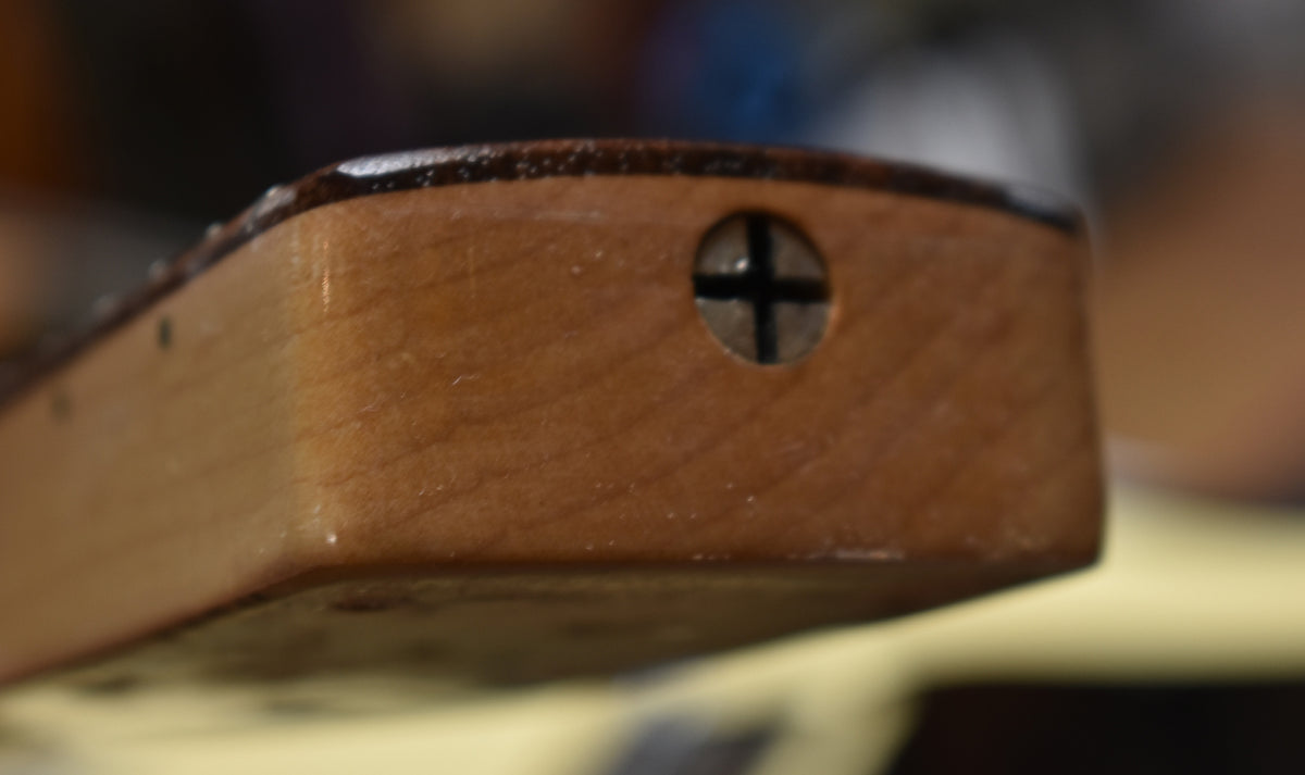 Close-up of the guitar neck heel, showing the wood grain, a Phillips head screw, and some finish wear along the top edge.