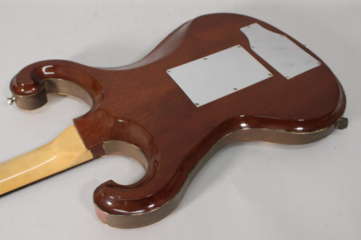 The back of a glossy dark brown guitar body with two silver control plates, showing wear along the edges and a light maple neck.