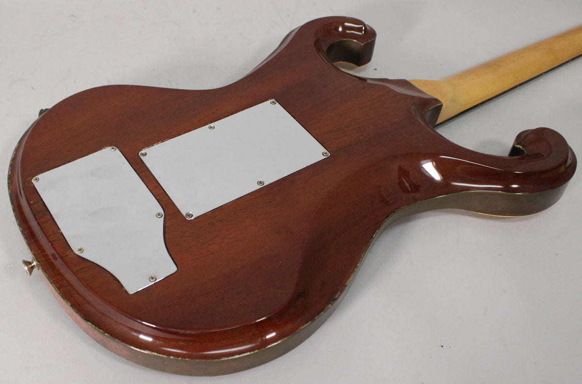 The back of a reddish-brown electric guitar, angled right, shows two silver control plates and wear along the edges.