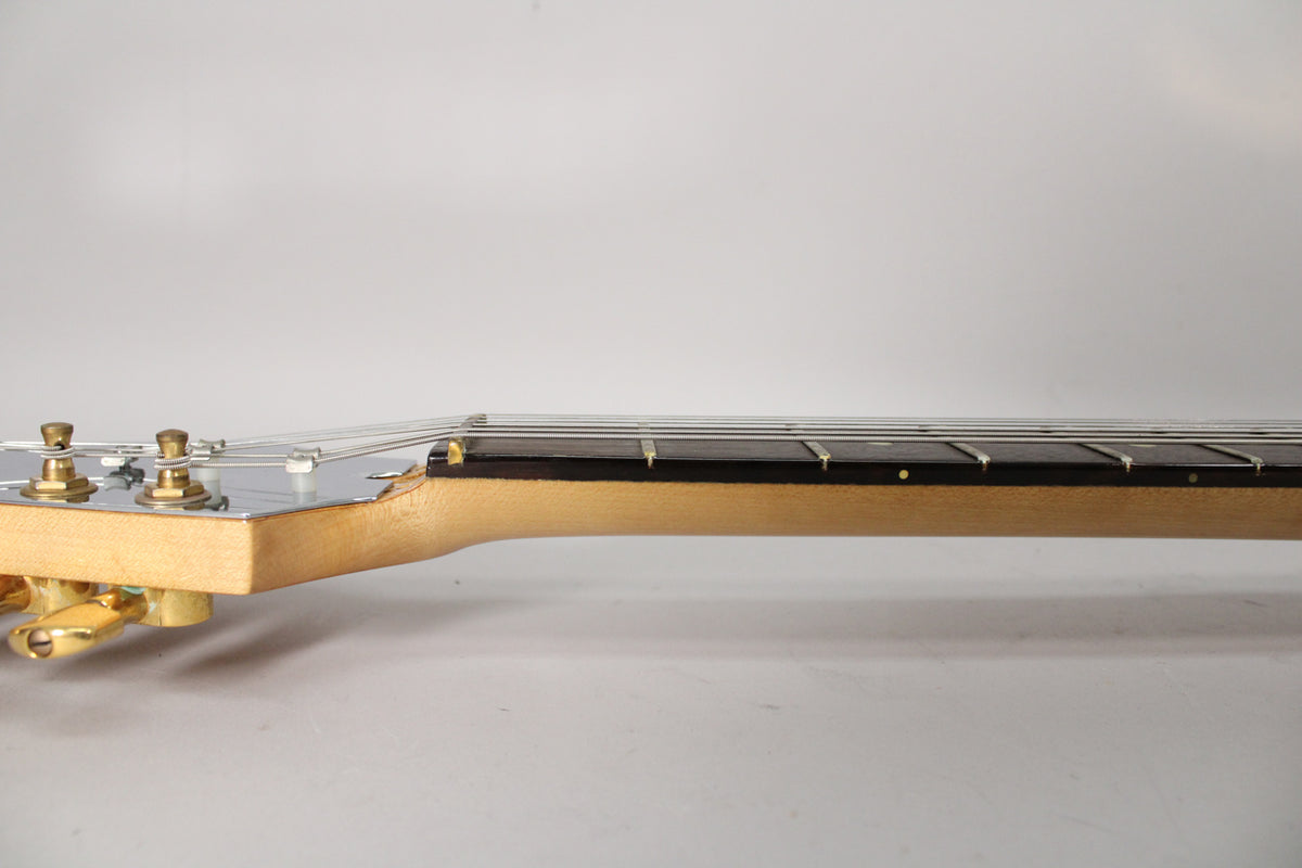 Side view of the guitar's headstock and neck, showing gold tuners, a chrome truss rod cover, and a dark fretboard with dot inlays.