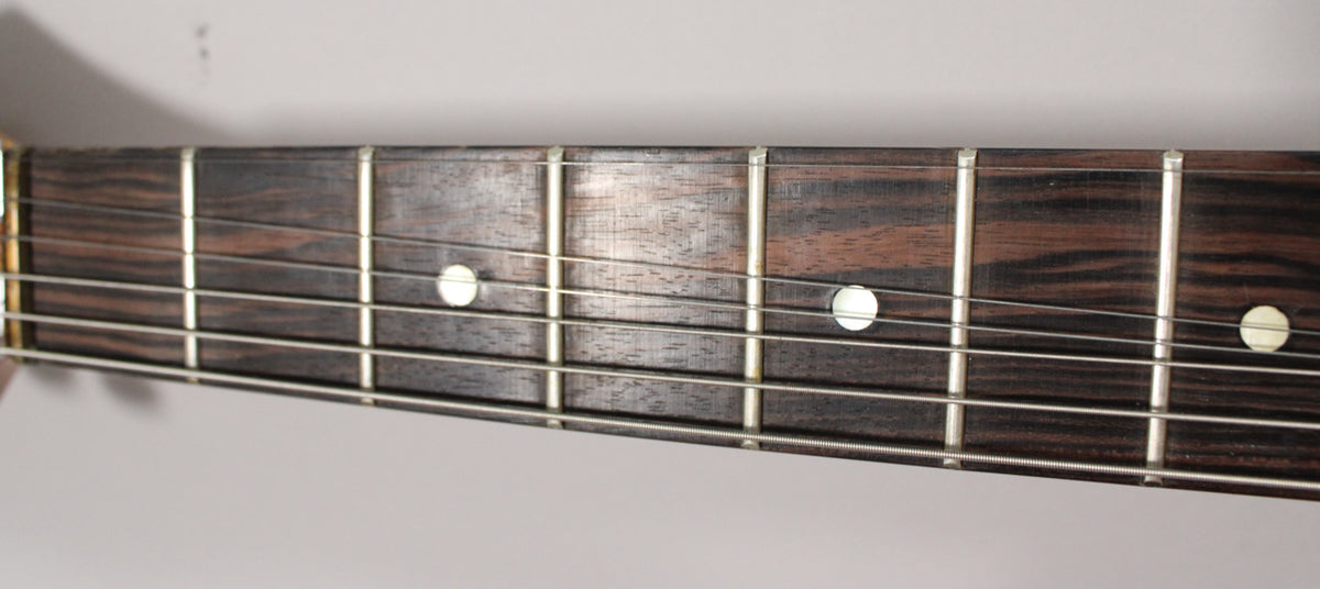 Close-up of the dark wood fretboard with light circular inlays and silver frets, showing light wear and string marks.