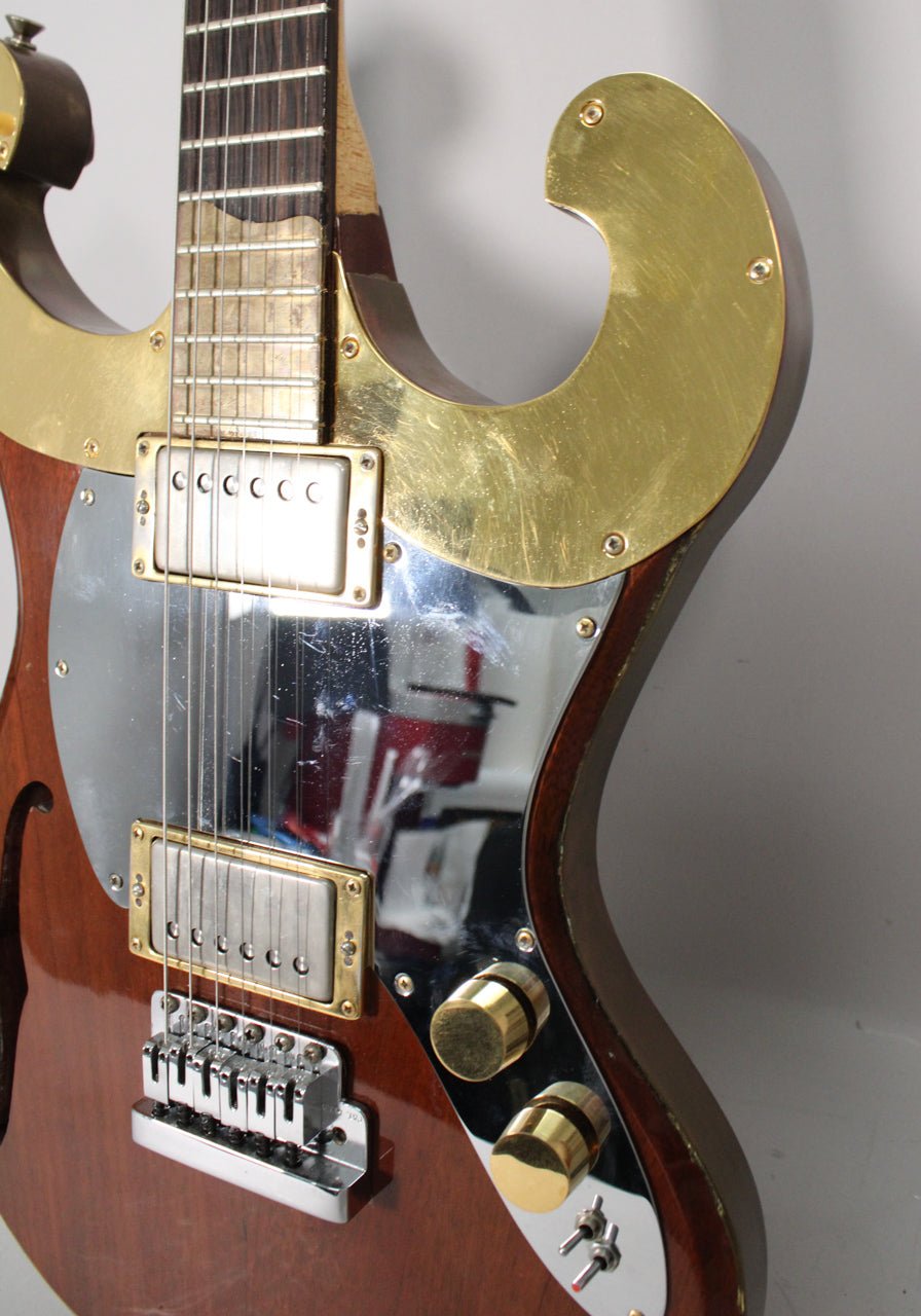 Close-up of a brown electric guitar with gold and chrome hardware, showing the fretboard, pickups, bridge, and control knobs.