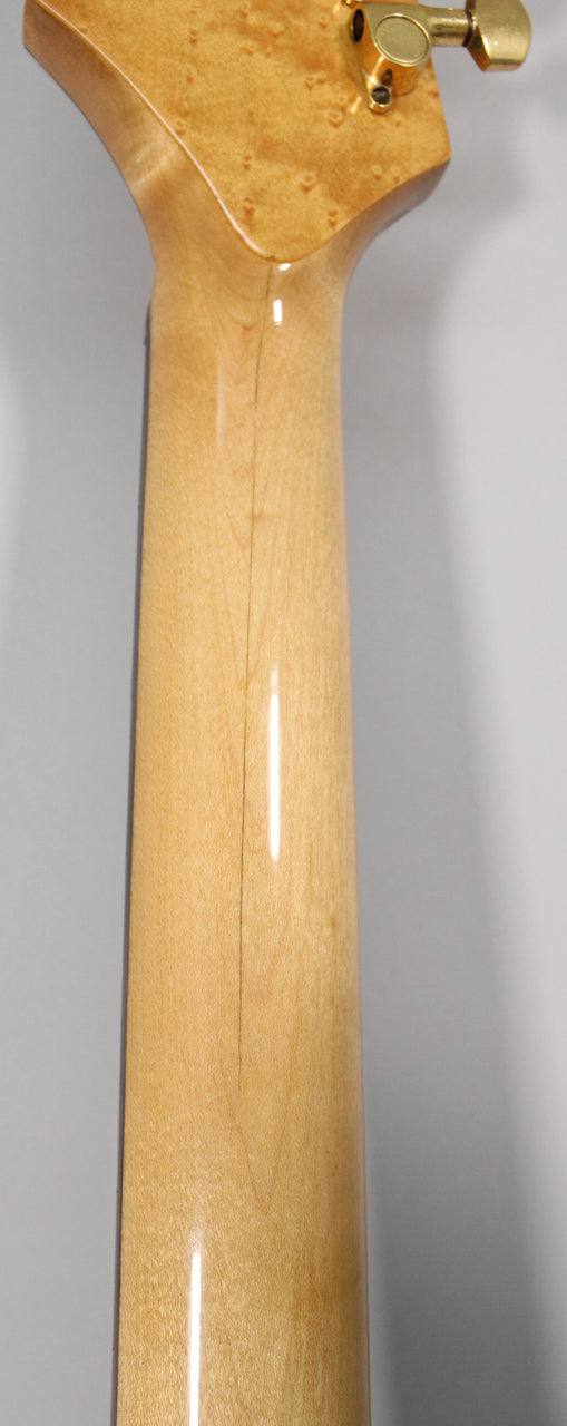 The back of the guitar's light wood neck and headstock, showing a vertical crack down the center and gold tuning pegs.