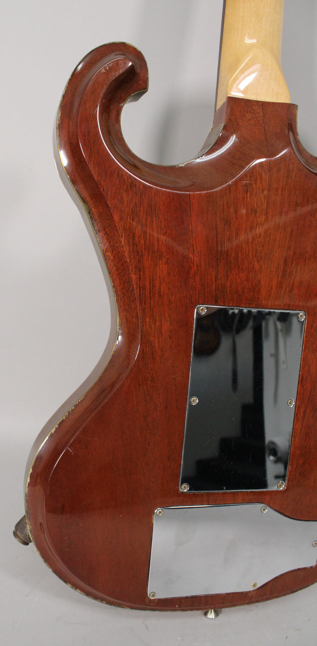 Rear view of the guitar's reddish-brown body, showing a black control plate, a chrome plate, and finish wear along the edges.