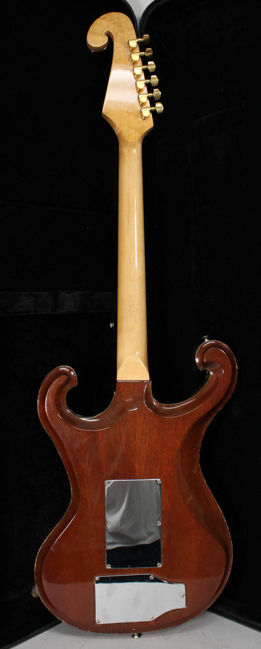 The back of the guitar shows a light wood neck with a scroll headstock and gold tuners, joining a dark brown body with chrome control plates.