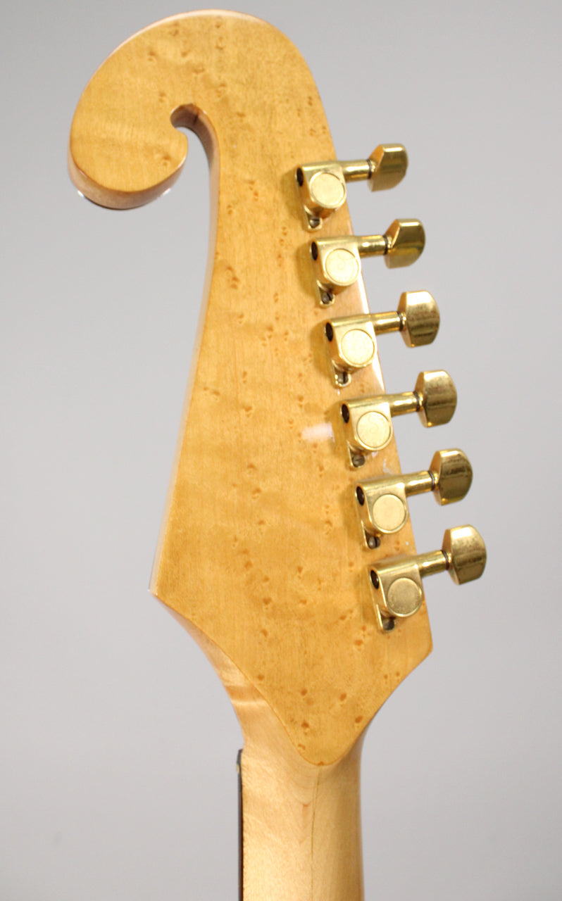 Close-up of the light-colored, curly maple headstock with a scroll-like top and six gold tuners, showing some finish wear.