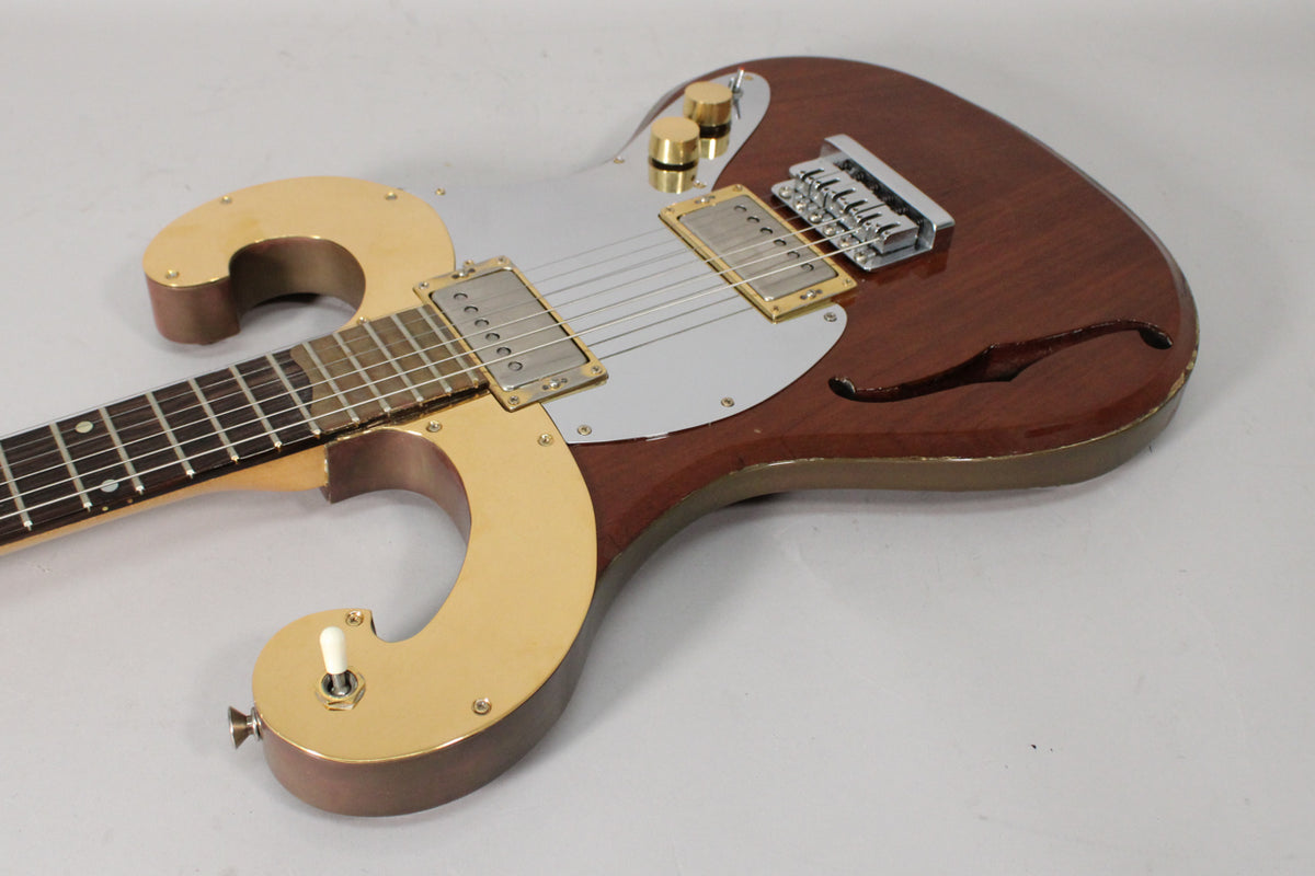 The brown semi-hollow guitar, angled right, shows a silver pickguard, gold hardware, and a small f-hole on the lower bout.