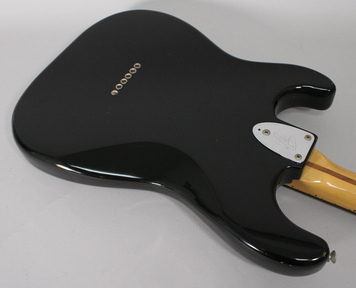 The black guitar body's back shows six gold string ferrules, a chrome neck plate, and a light wood neck with a dark stripe.