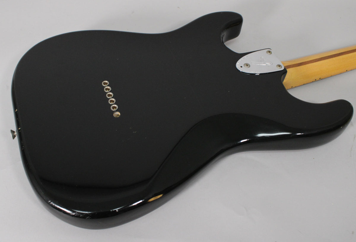 The black guitar body's back, angled from the lower bout, shows six string-through ferrules and a chrome neck plate.