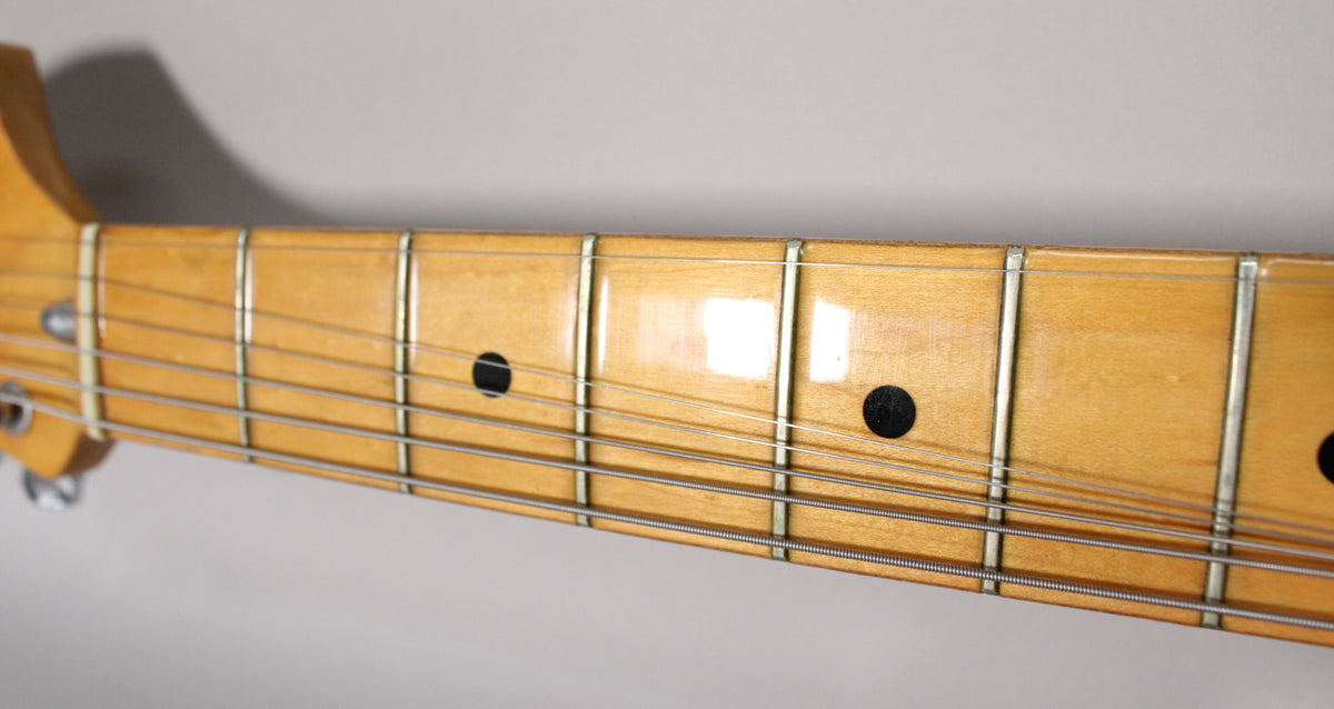 Close-up of the maple fretboard, showing black dot inlays, frets, and strings, with some visible wear on the finish.