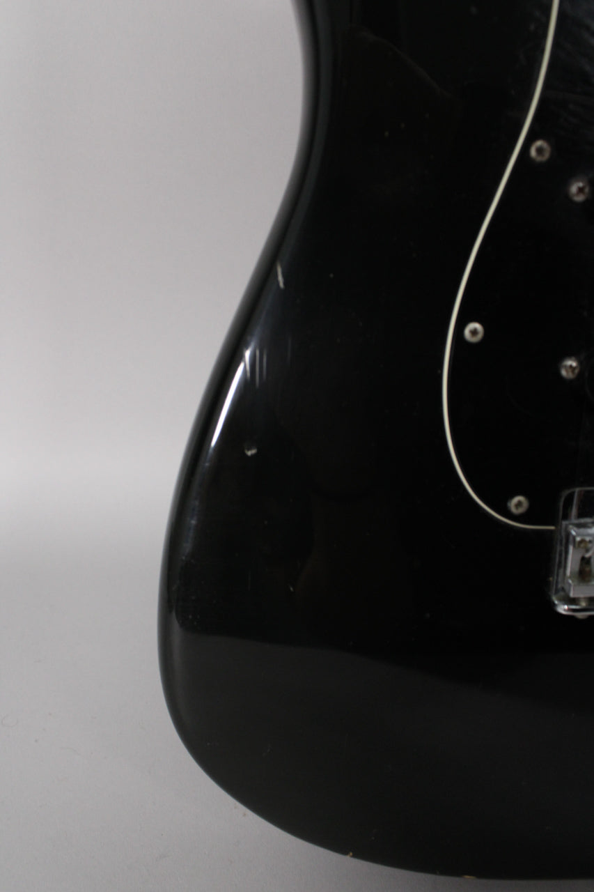 Close-up of the black guitar body's lower bout, showing light scratches and a small ding on the glossy finish, with part of the pickguard visible.