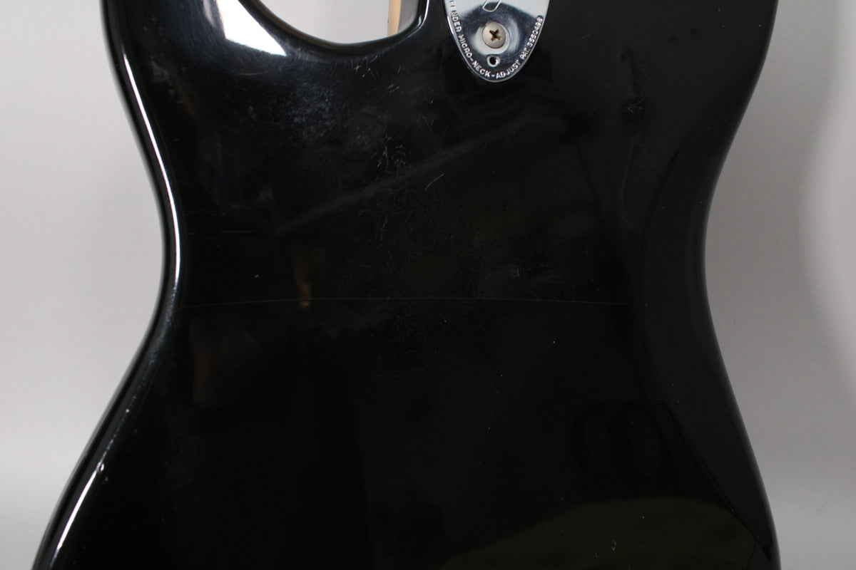 The upper back of a glossy black guitar body, showing light scratches and a neck plate with a visible screw.