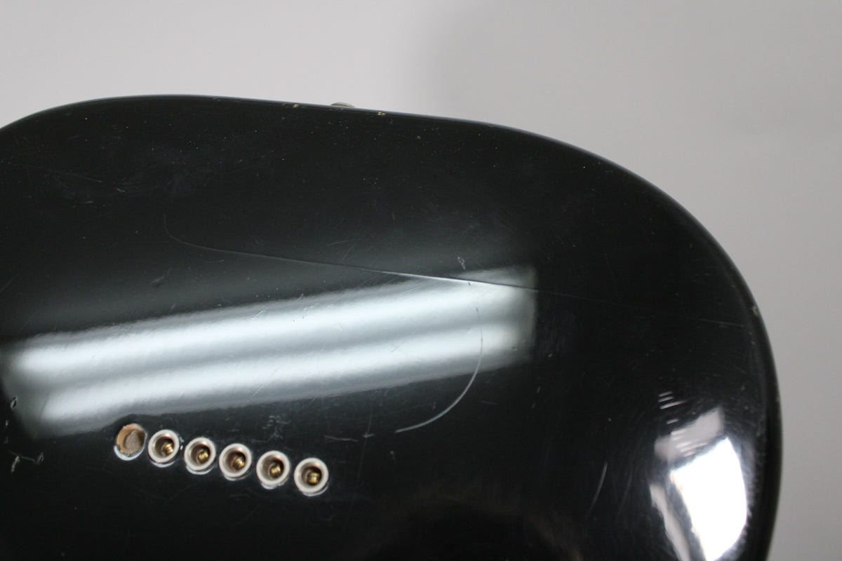 Close-up of the black guitar body's lower bout, showing six gold string-through-body ferrules and light surface scratches.