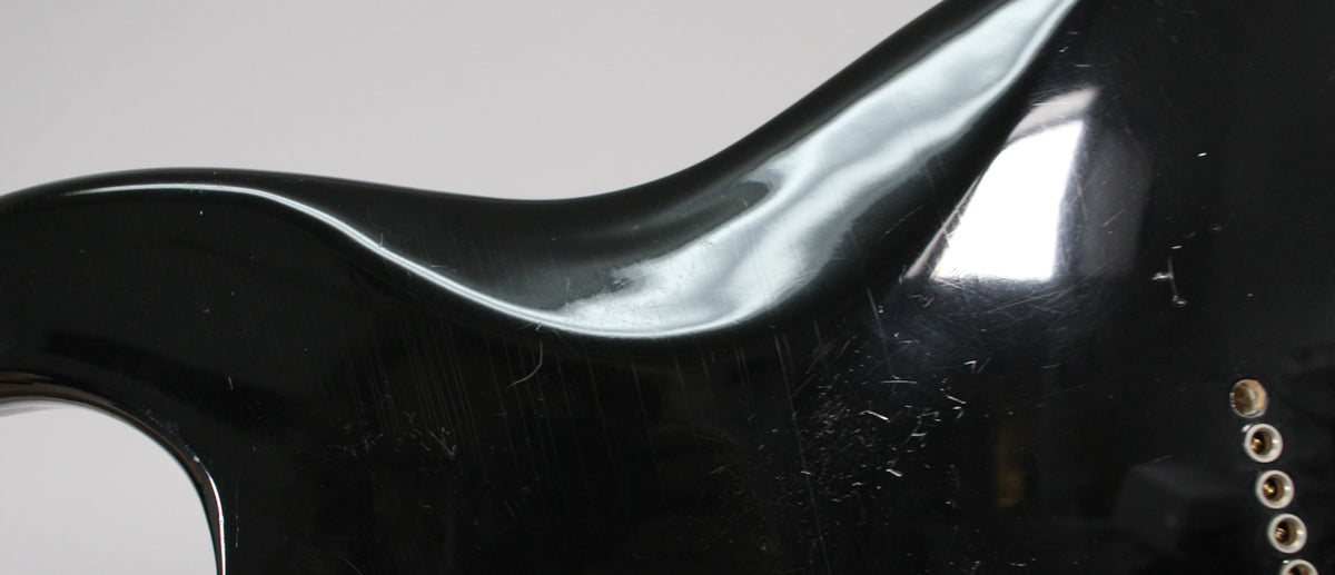 Close-up of the guitar's upper horn and waist, showing many light scratches and scuffs on the glossy black finish.