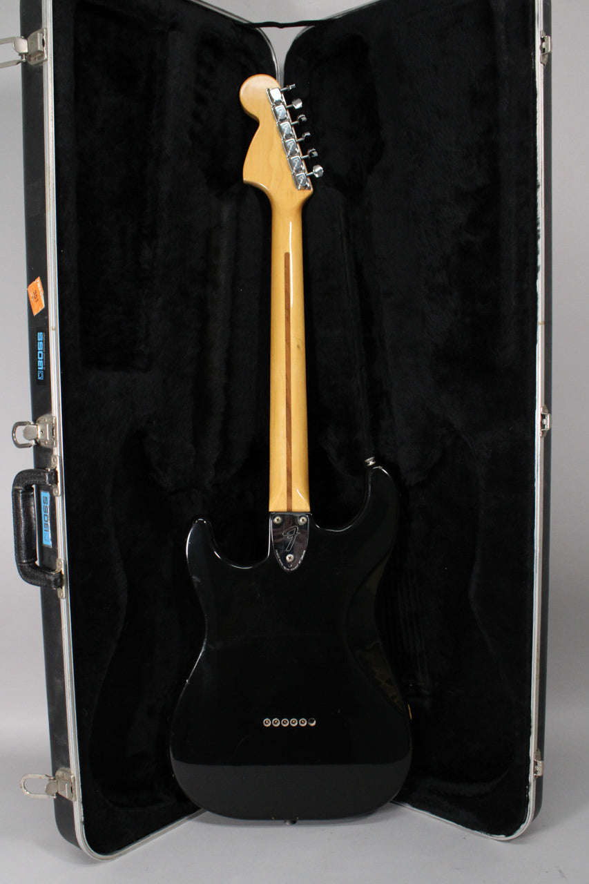 Full rear view of a black Stratocaster with a maple neck, chrome tuners, and a six-saddle hardtail bridge, resting in a black hard case.