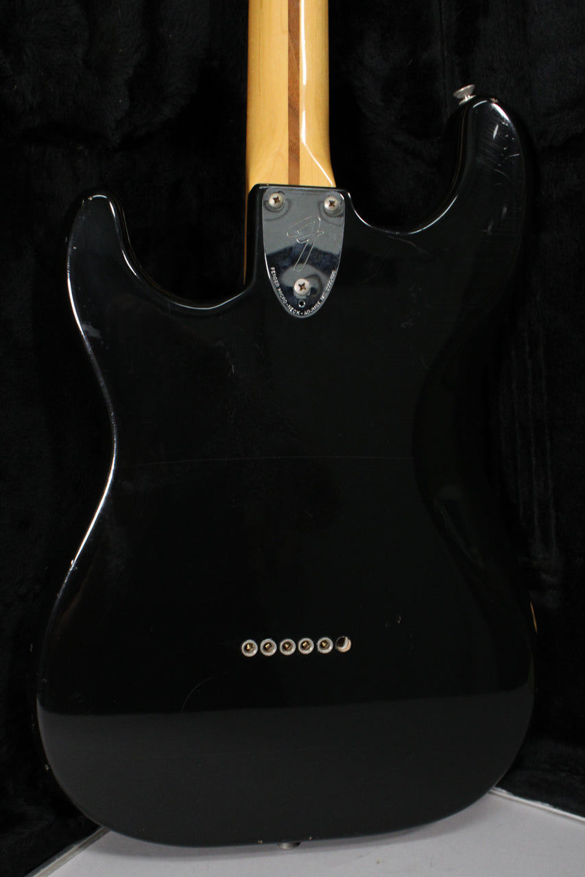 The back of a black Stratocaster shows a maple neck, chrome neck plate, six string-through-body ferrules, and light surface scratches.