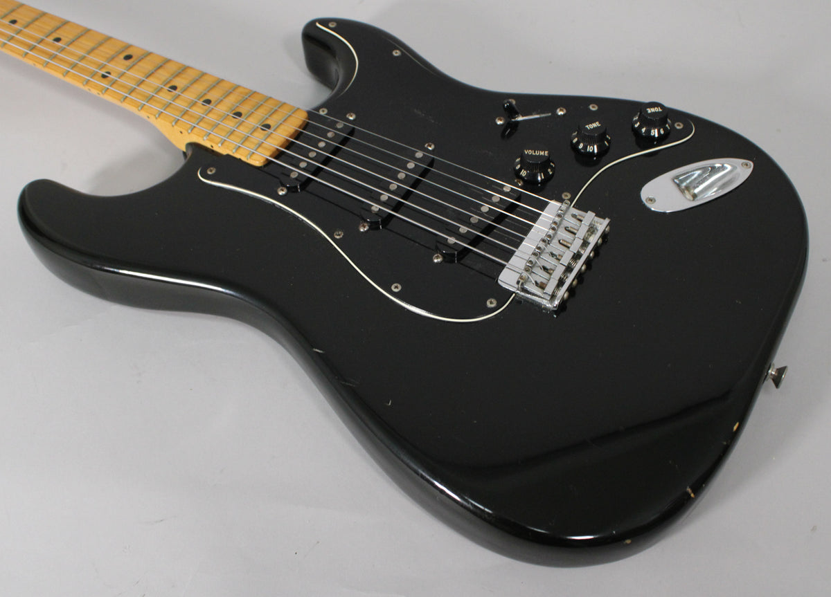 Black hardtail Stratocaster, angled from the lower bout, showing a maple neck, black pickguard, three single-coil pickups, and chrome bridge.