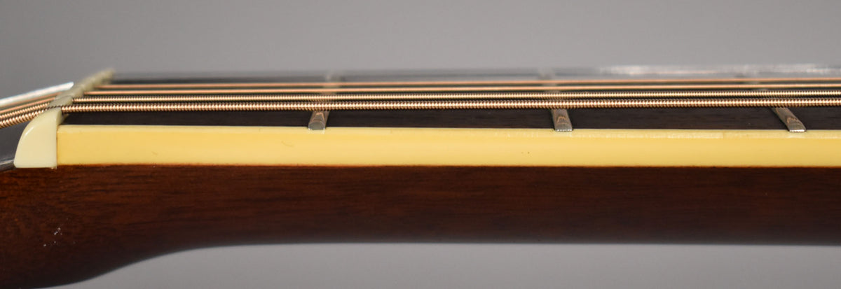 Close-up of the guitar's dark brown neck and fretboard, with a cream-colored binding and six bronze strings.