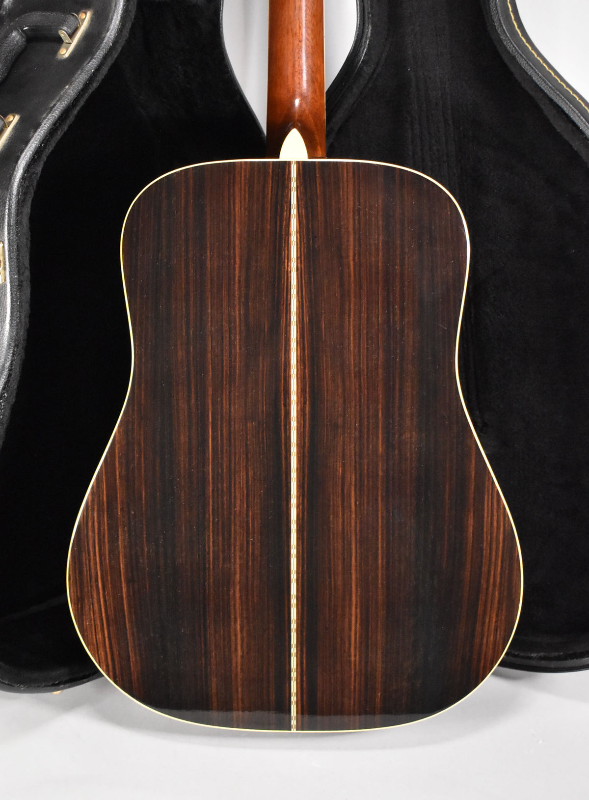 The guitar's dark, striped wood back with a light center strip and binding is visible, with the neck heel and open case behind it.