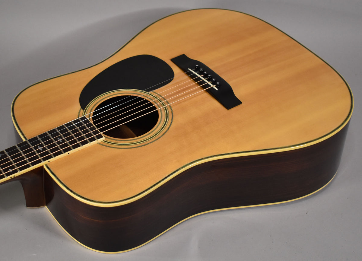 The natural finish acoustic guitar is angled from the left, showing its light top, dark sides, black pickguard, and bridge.