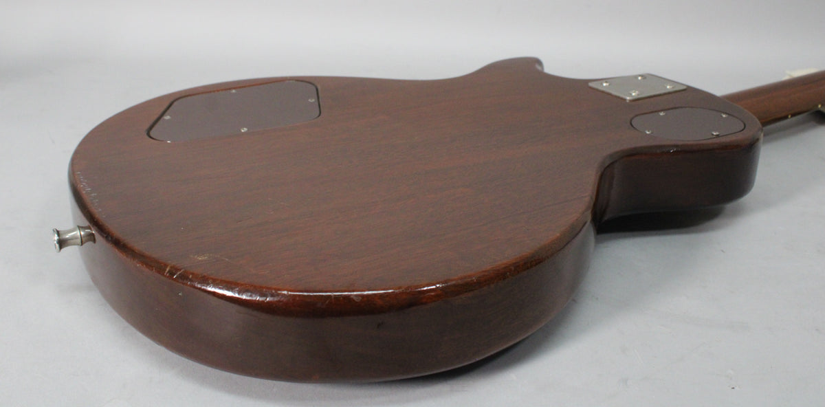 The back of a dark brown guitar body, showing two control cavity covers and a chrome neck plate, with wear along the edges.