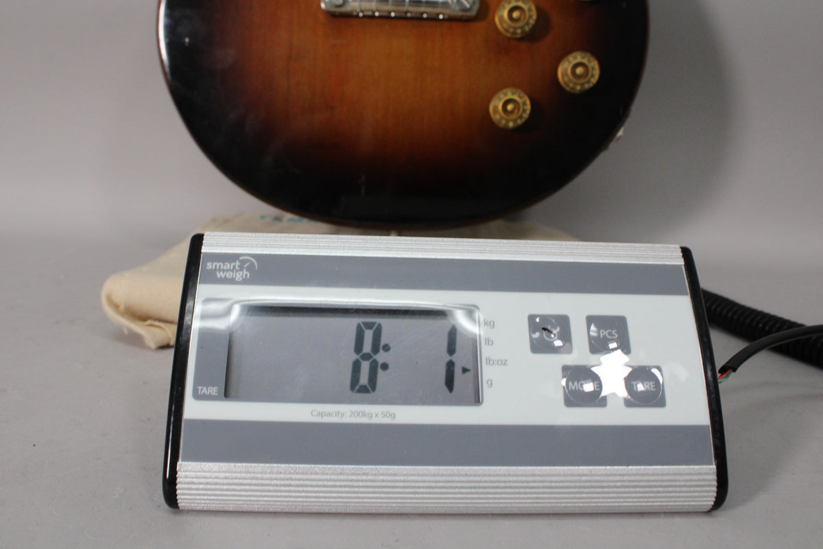 The guitar's lower body in tobacco sunburst finish is visible above a digital scale displaying "8.1" lbs.